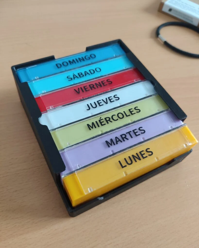 Los siete cajetines de un pastillero semanal, metidos en una bandeja negra impresa en 3D.