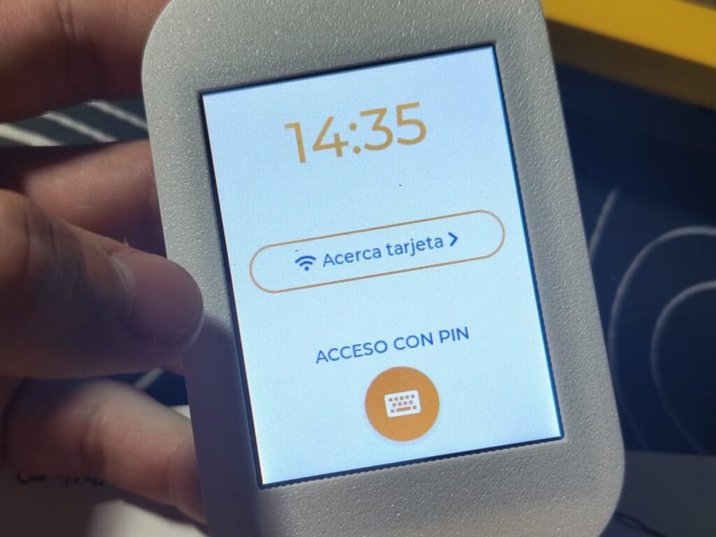 Carcasa gris impresa en 3D sujetando una pantalla tactil que muestra la hora y un acceso con tarjeta o PIN.