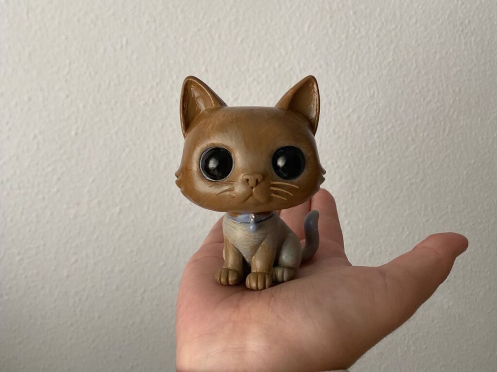 Figura de un gato marrón con los ojos grandes, sostenida en la palma de una mano.