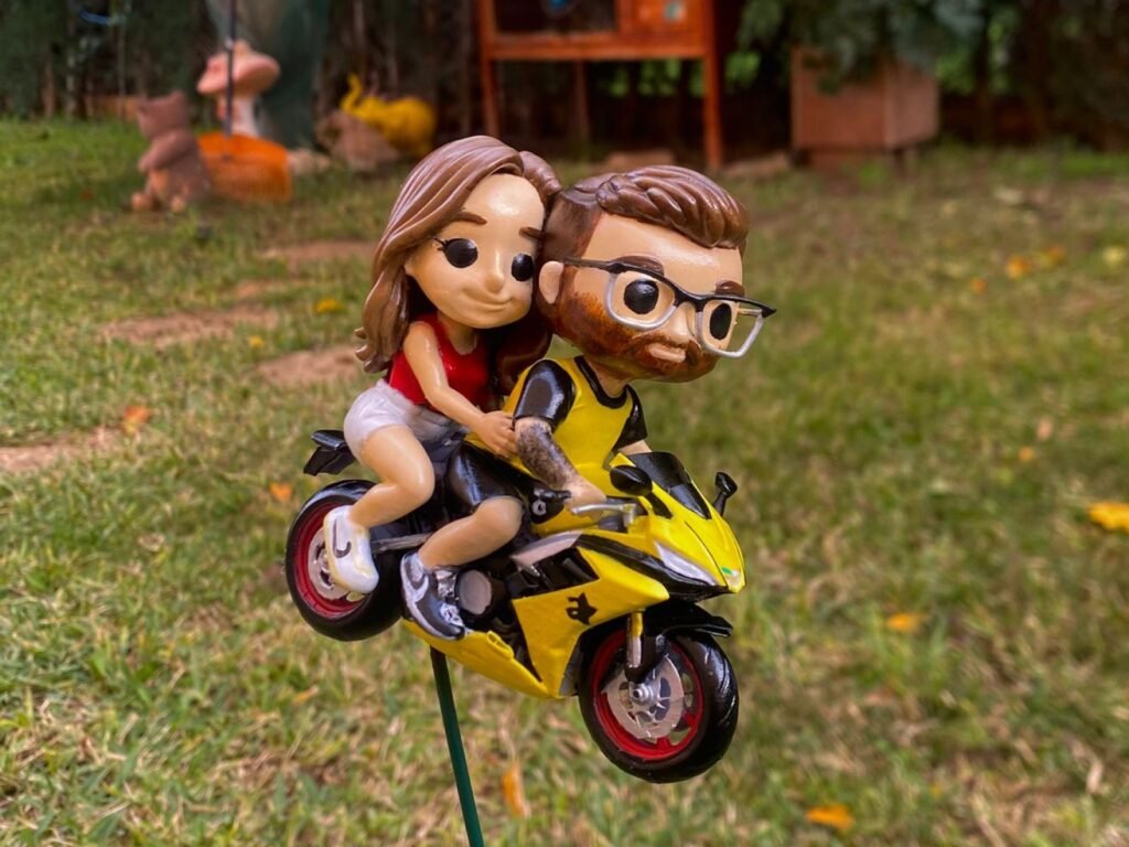 Figura de una pareja montada en una moto amarilla, pintada a mano, sobre el césped de un jardín.