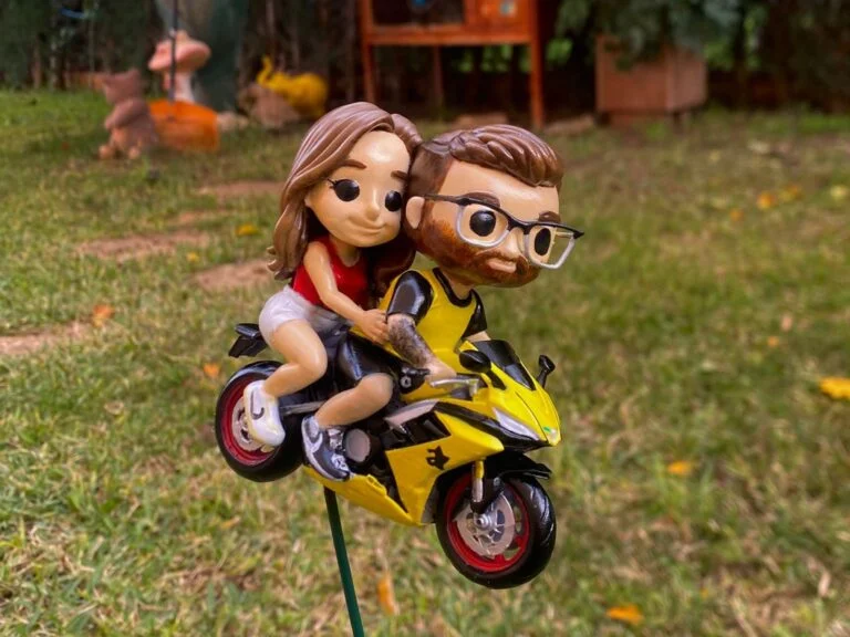 Figura de una pareja montada en una moto amarilla, pintada a mano, sobre el césped de un jardín.