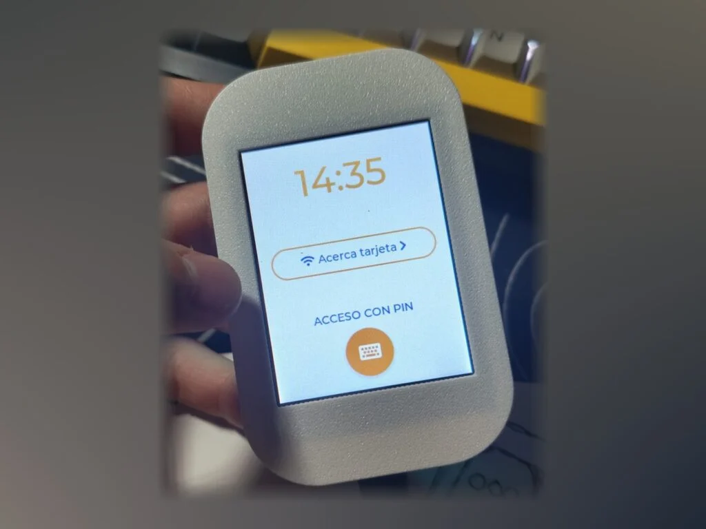 Carcasa gris impresa en 3D sujetando una pantalla tactil que muestra la hora y un acceso con tarjeta o PIN.