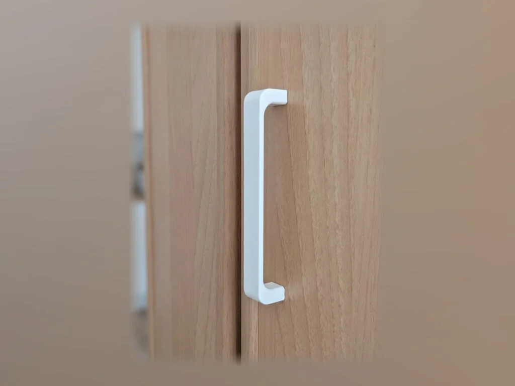 Tirador blanco impreso en 3D montado en la puerta de un armario de madera clara.